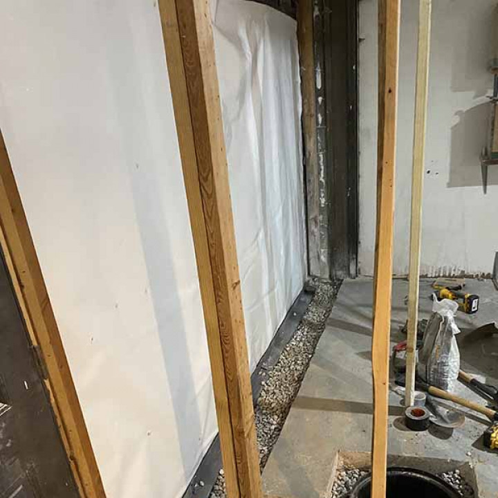 exposed framing and drywall in an unfinished basement during the preparation for waterproofing