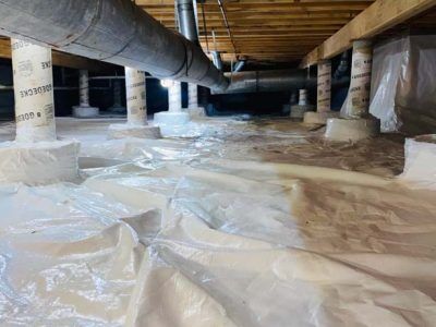 A crawl space with a plastic vapor barrier covering the ground, support columns, and exposed ductwork overhead.