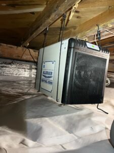 a dehumidifier strapped to a floor beam in the crawlspace