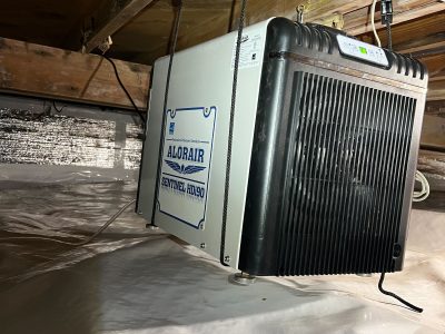 a dehumidifier strapped to a floor beam in the crawlspace