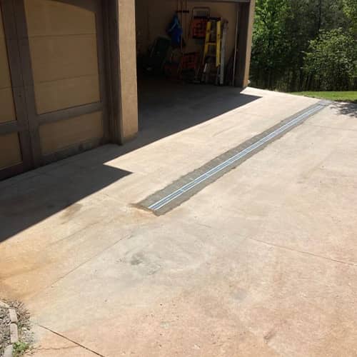 A drainage line beneath a concrete driveway