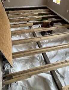 A person is installing floor joists over a plastic moisture barrier in a room under renovation.