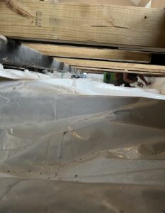 A person works under wooden beams with plastic sheeting covering the ground, suggesting construction or renovation activity.