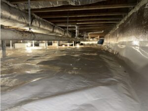 A crawl space with a plastic vapor barrier covering the floor and insulation on the walls and pipes, with exposed wooden joists above.