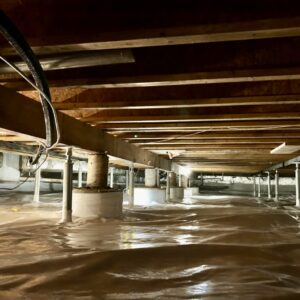 Crawl space with exposed wooden beams and pipes, supported by columns, with a plastic moisture barrier covering the ground.