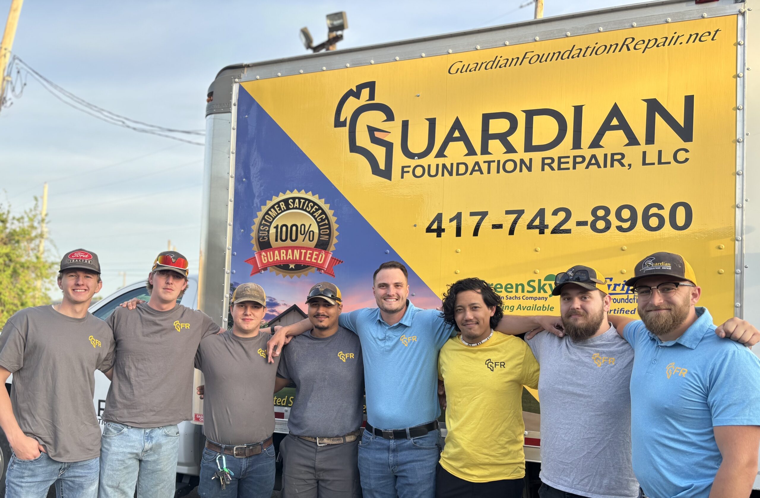 A group of seven men stand in front of a Guardian Foundation Repair truck, all wearing company shirts and posing for a group photo.