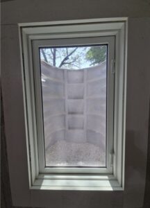 A window looking out to a concrete window well with gravel at the bottom and a small section of tree branches visible above.