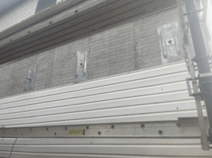 A close-up view of a building exterior under construction, showing insulation panels, metal brackets, and partially installed siding.