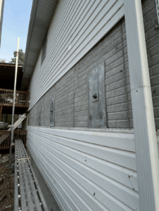 A brick wall with several large metal anchor plates and partially removed vinyl siding, next to scaffolding on the side of a house.
