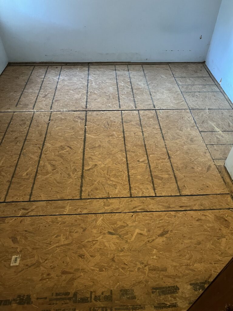 Room with bare chipboard flooring marked with black lines in a grid pattern. White walls and no furniture.