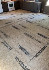 Kitchen with brown cabinets and stove; plywood subfloor exposed, showing construction markings and fasteners.
