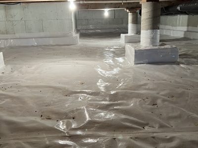 A crawl space with a clean, white vapor barrier covering the floor and structural supports, illuminated by overhead lights.