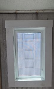 A small window with a white frame set in a concrete wall, with light coming through a frosted or covered glass pane.