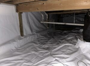 A crawl space with plastic sheeting covers the floor and parts of the walls, visible pipes, and wooden beams overhead.