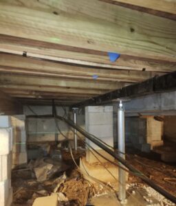 Crawl space with exposed wooden floor joists, concrete block piers, metal support posts, and visible electrical wiring.