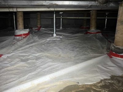 Crawl space with white plastic ground covering, wrapped pillars, and visible pipes.