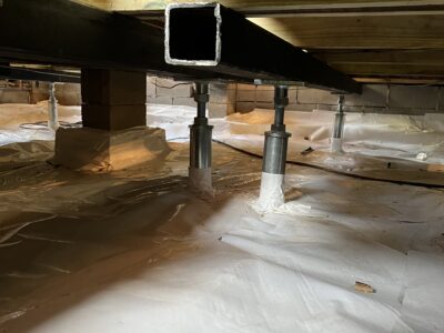 Crawl space with white vapor barrier lining and steel support beams.