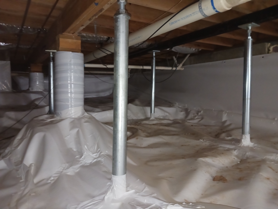 Crawl space with support columns, pipes, and a white tarp covering the floor and walls.